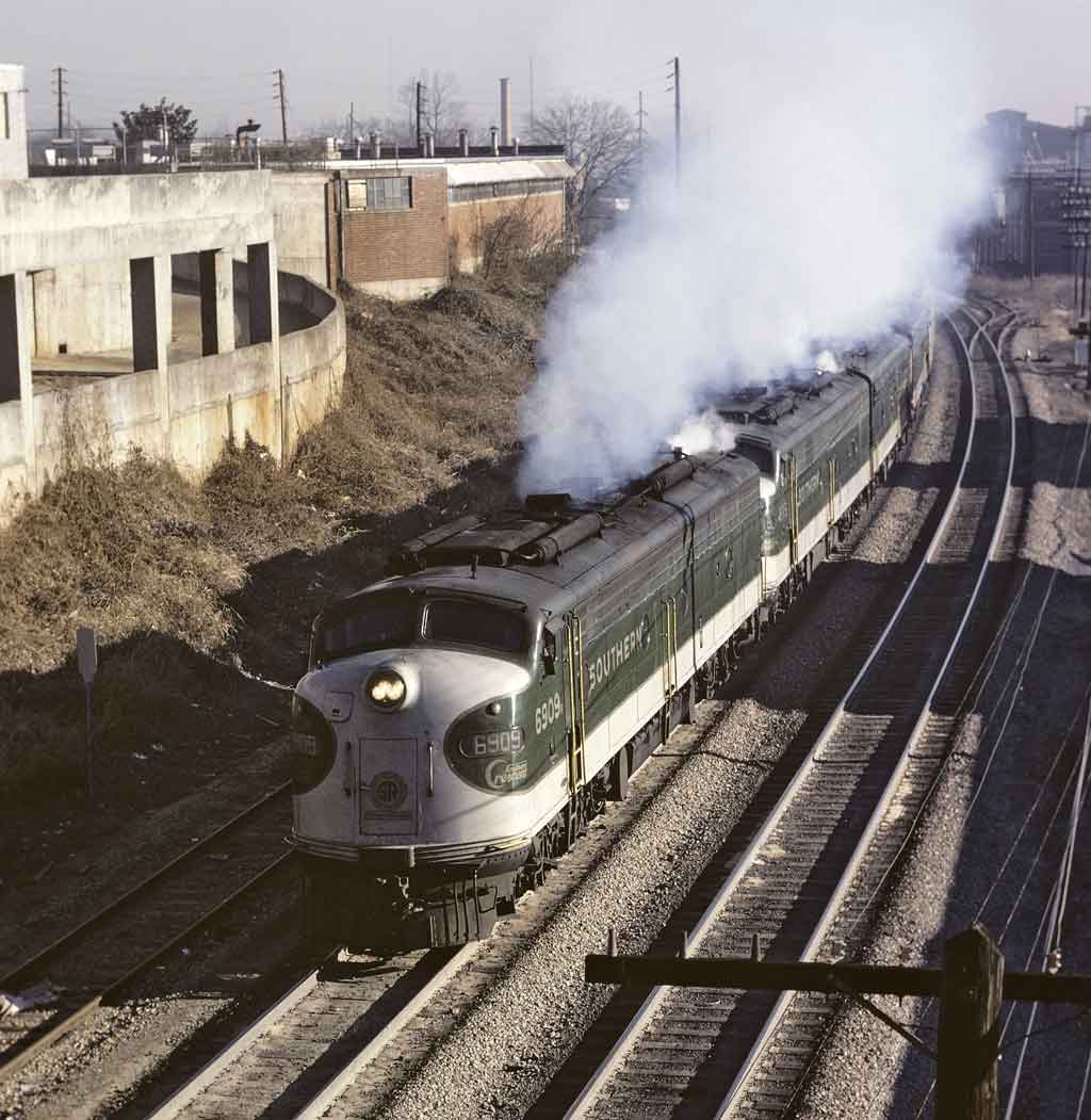A green and white locomotive leaving a train station