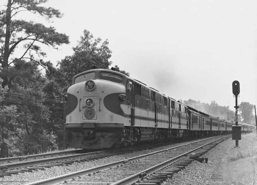 A black and white photo of a locomotive passing a stop light