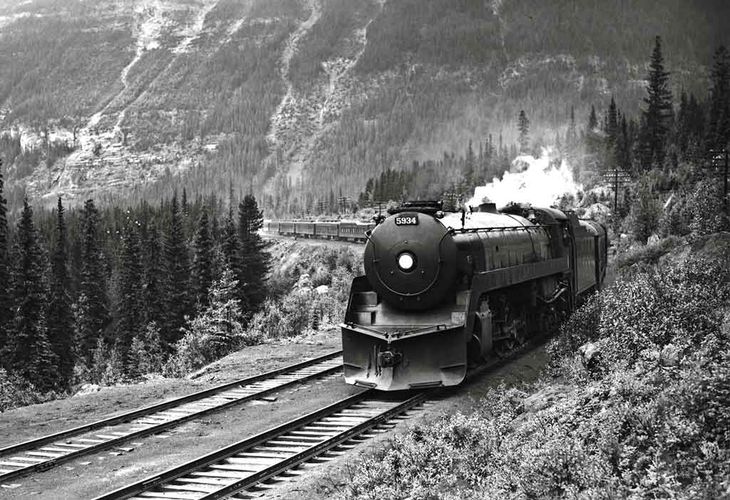 Streamlined steam locomotive on passenger train in wooded mountains