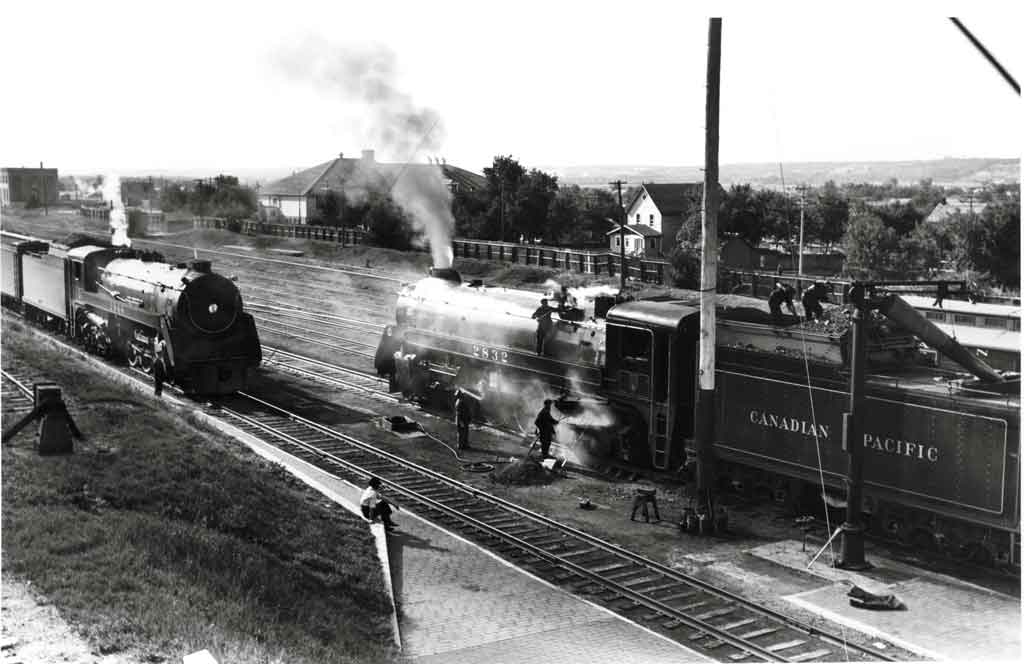 Men work on a steam locomotive while a second approaches