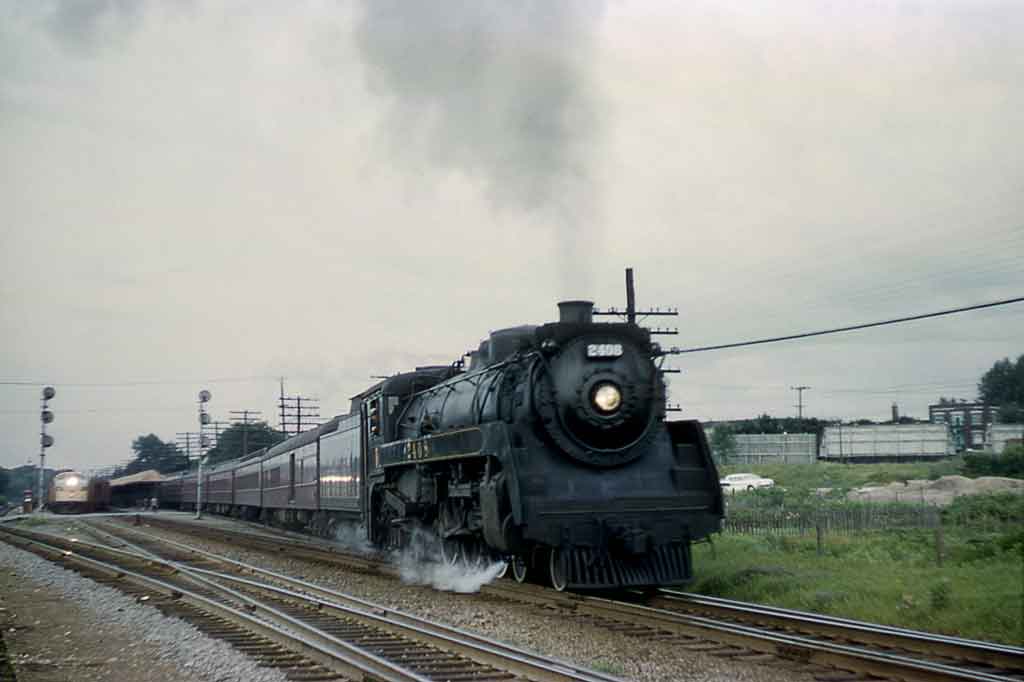 Steam locomotive departing station with train with diesel in distance