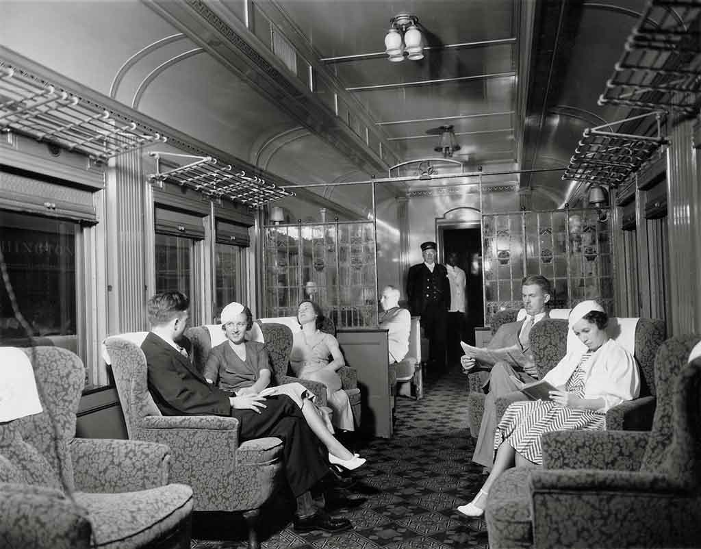 A black and white photo of passengers sitting in a lounge car