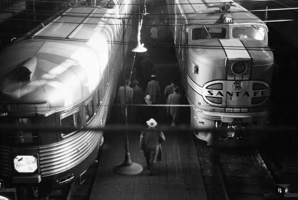 A black and white overhead shot of passengers walking to a train