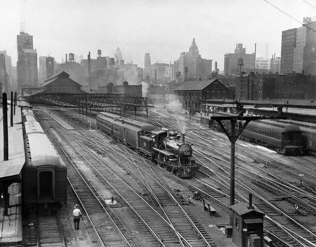 A black and white distant and overhead shot of a train leaving a station
