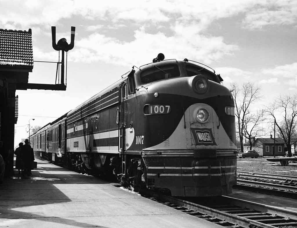 A black and white photo of a locomotive picking up passengers at a station
