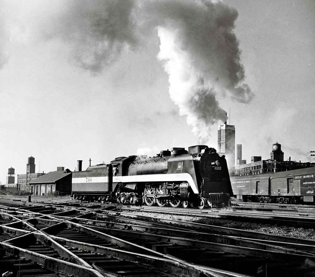 A black and white photo of a locomotive with white smoke coming out of its chimney