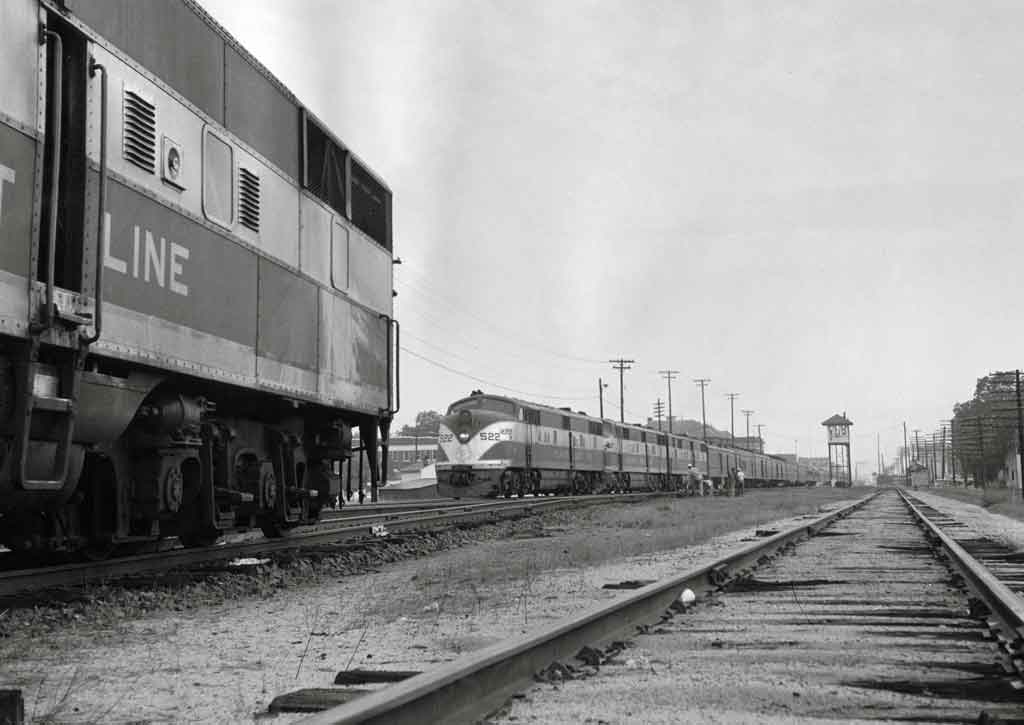 a diesel passenger train rolling up to an E unit in the foreground
