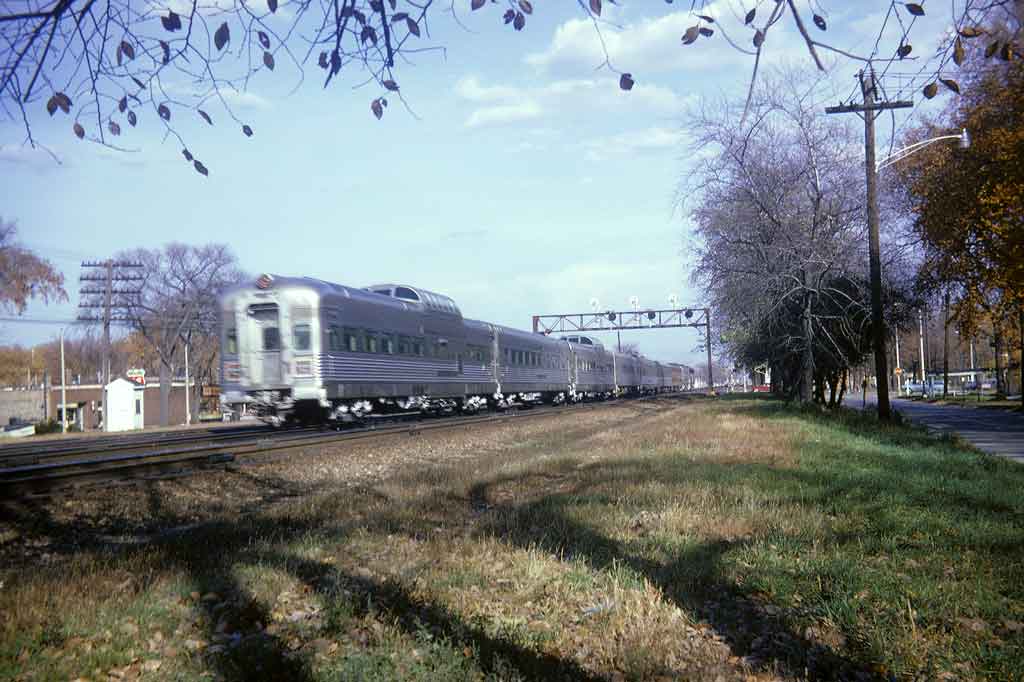 A silver train passing underneath a stop light