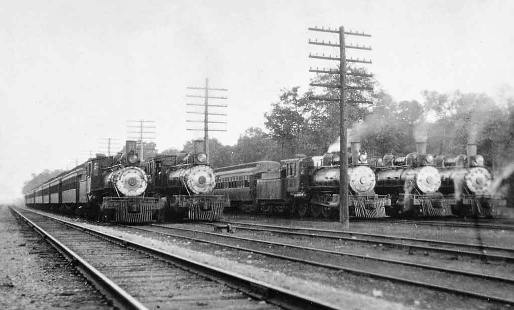 A black and white photo of five trains sitting in a rail yard