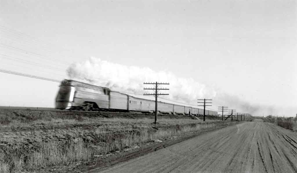 A black and white photo of a train traveling through a rural area
