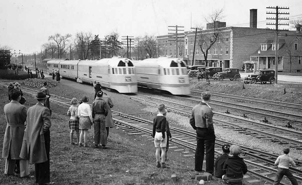 A black and white photo of a group of people watching two passenger trains go by
