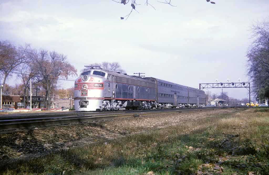 A silver train passing underneath a stop light