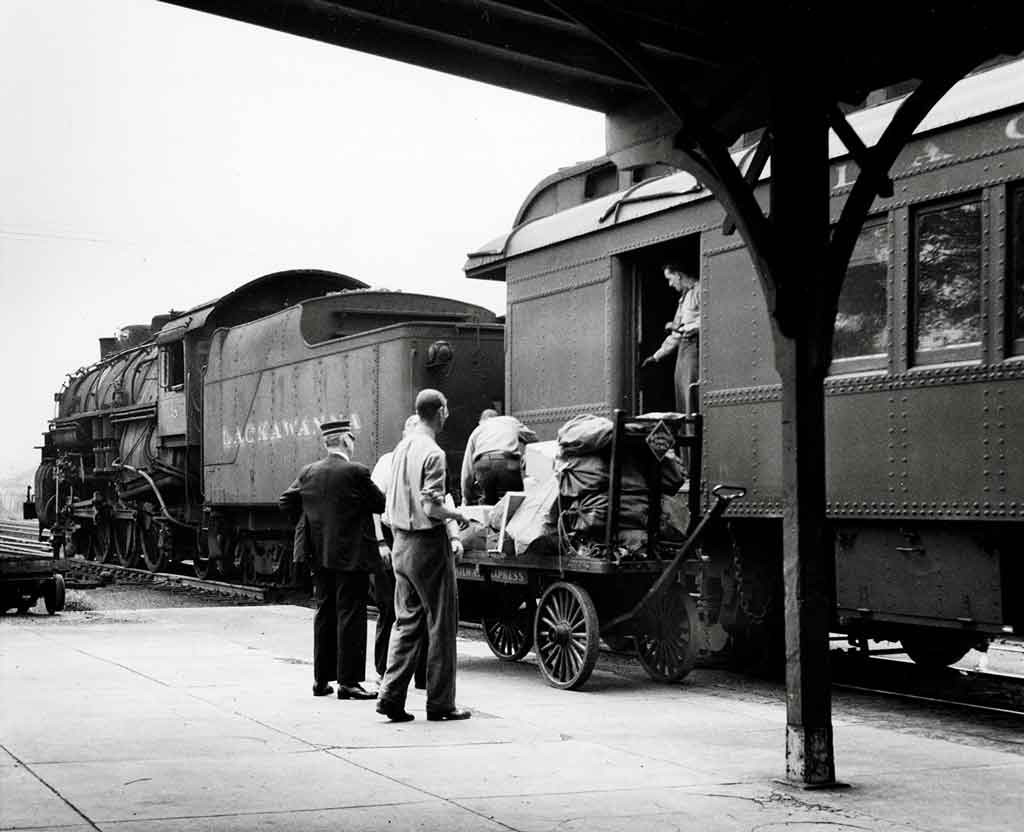 people loading baggage into a baggage car at a depot