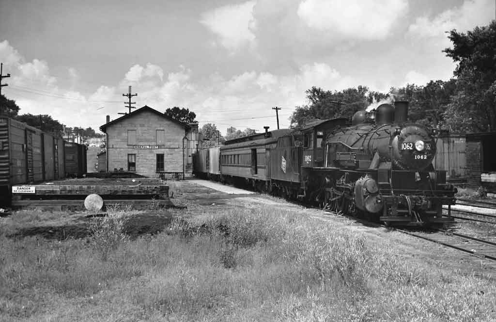 A black and white photo of a train traveling past a building