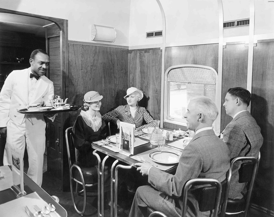 A black and white photo of four people being served food inside a train