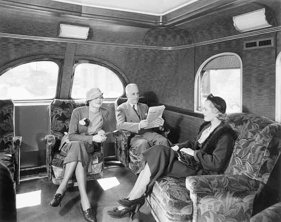 A black and white photo of three people talking inside a train
