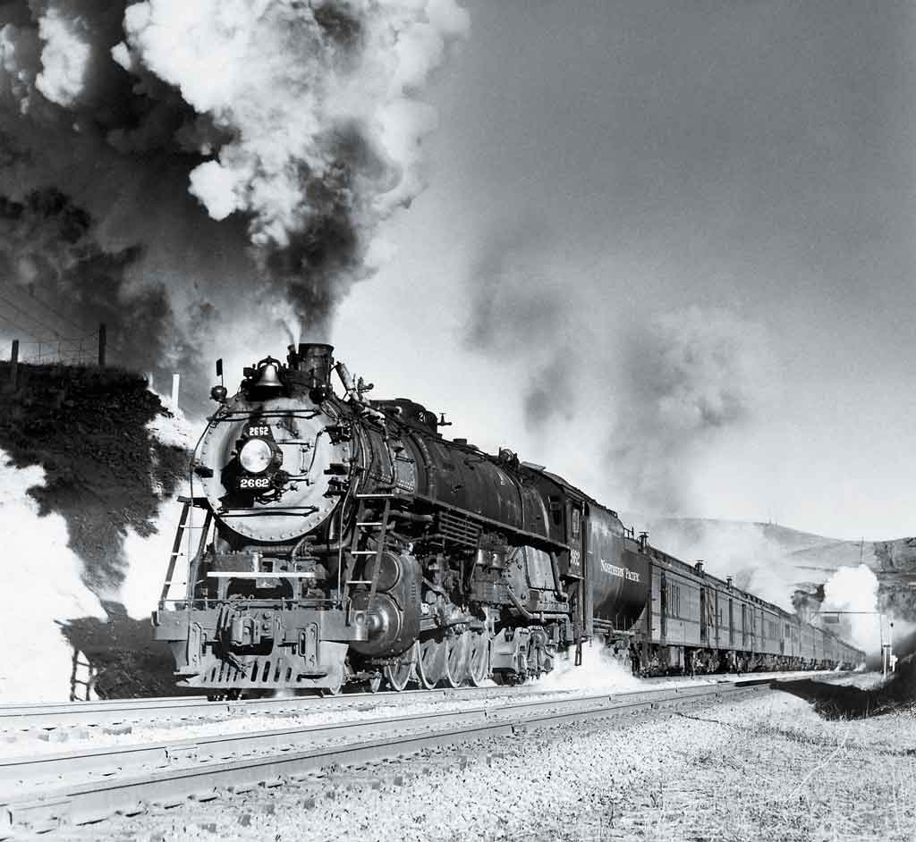 A close up black and white photo of a locomotive with smoke coming out of its chimney