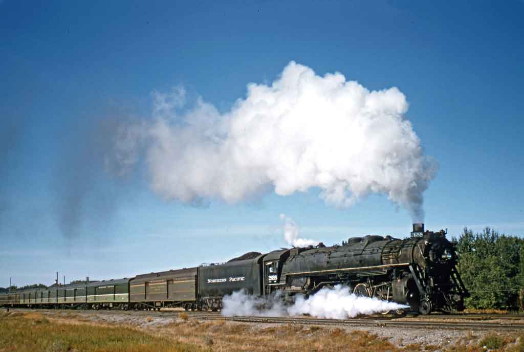 A locomotive on the track with big white smoke coming out of its chimney