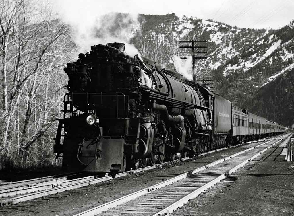 A black and white photo of a locomotive coming out of the mountains