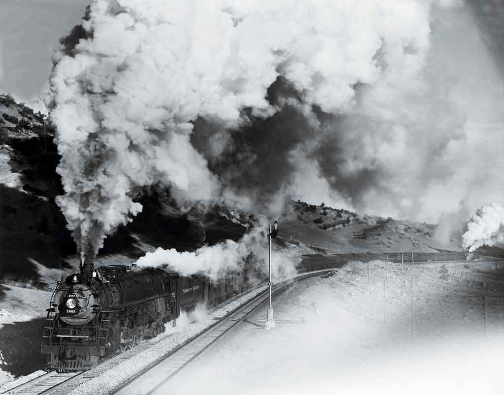 A black and white photo of a train with big white smoke coming out of its chimney
