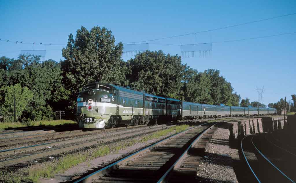 A green and white train passing by trees