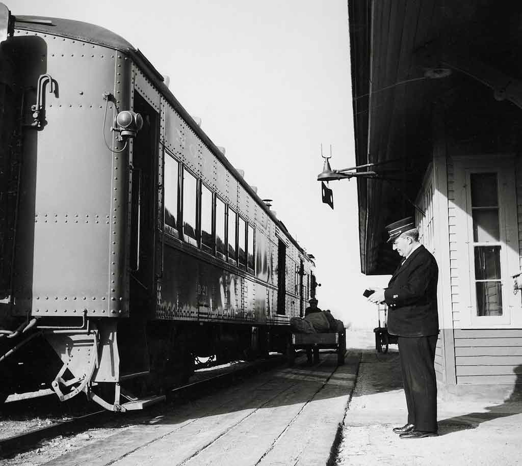 A black and white photo of the train conductor standing outside at the train station