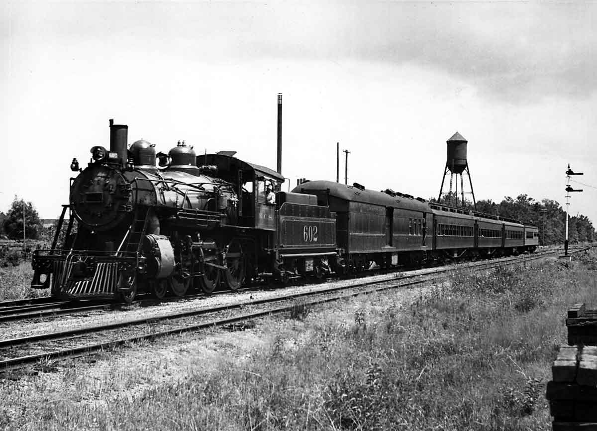 Steam locomotive with five passenger cars by semaphore signal and water tower
