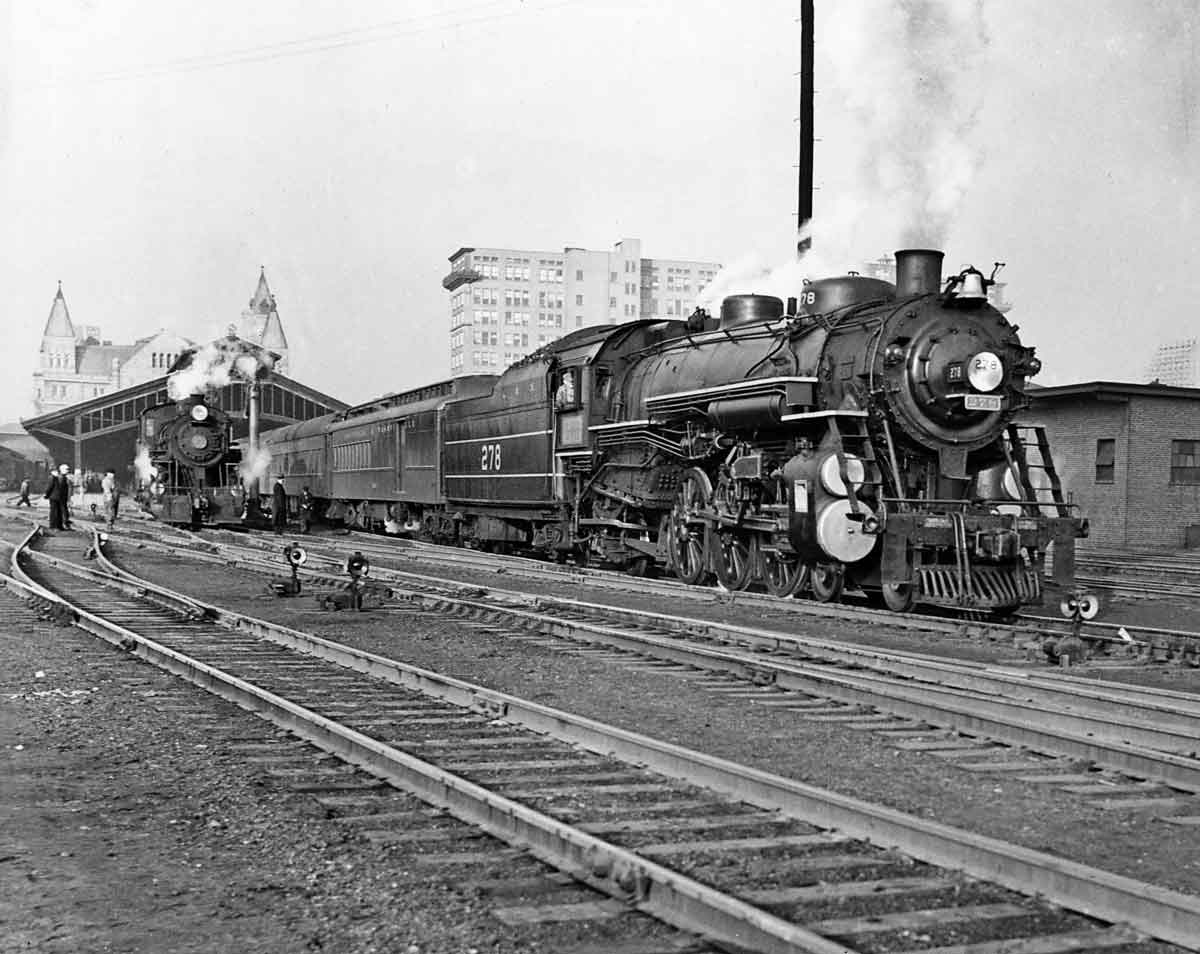A black and white photo of two trains passing through a station