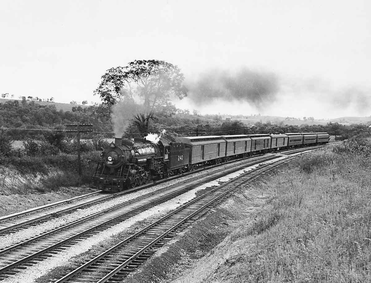 A black and white photo of a train turning a corner with smoke coming out of its chimney