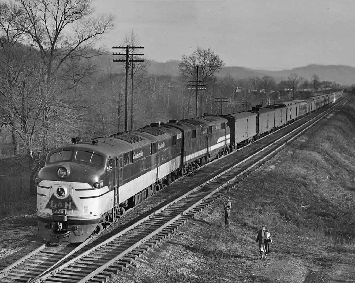 A black and white photo of a train passing by two people