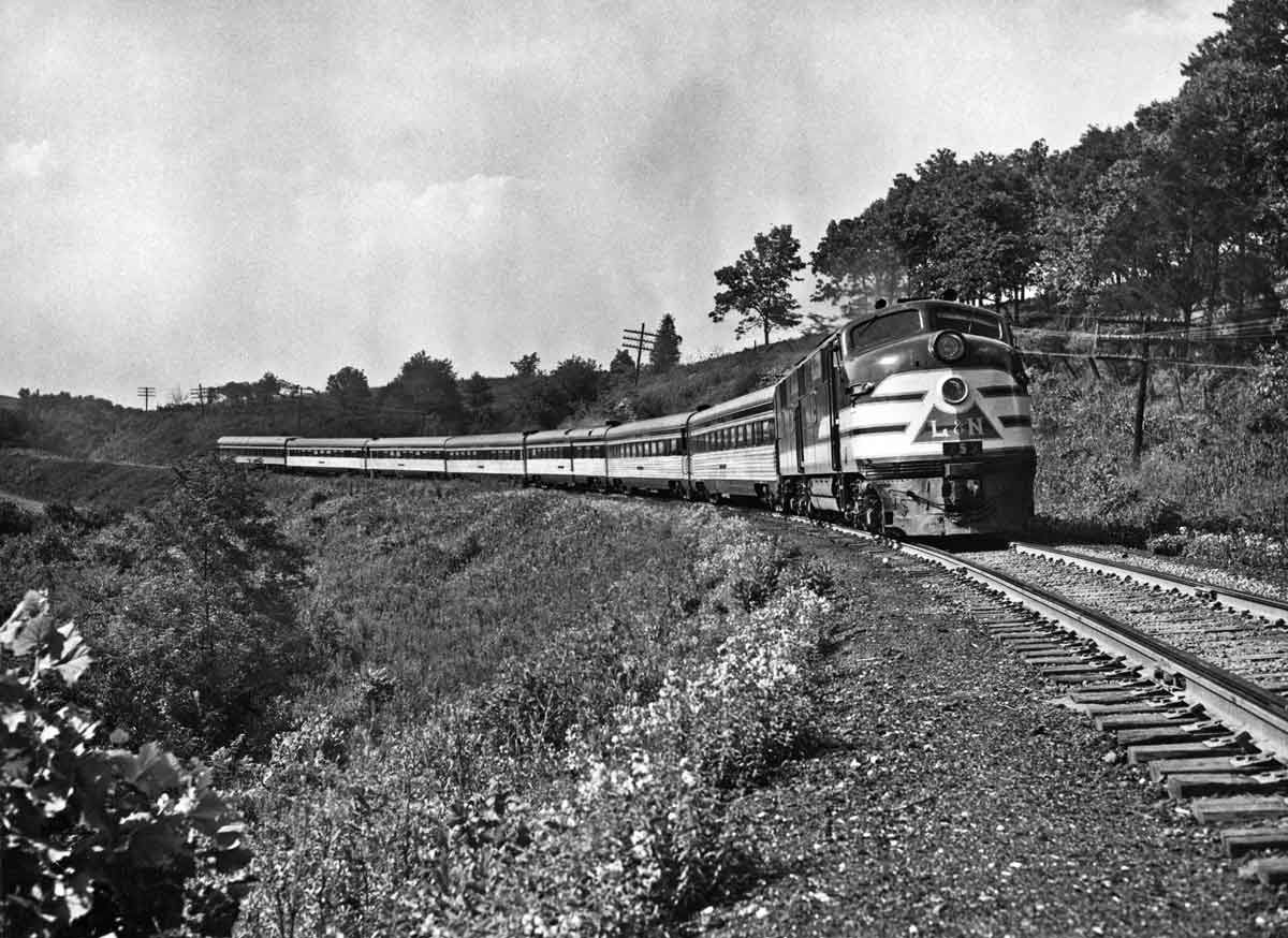 A black and white photo of a train turning a corner in a grassy area