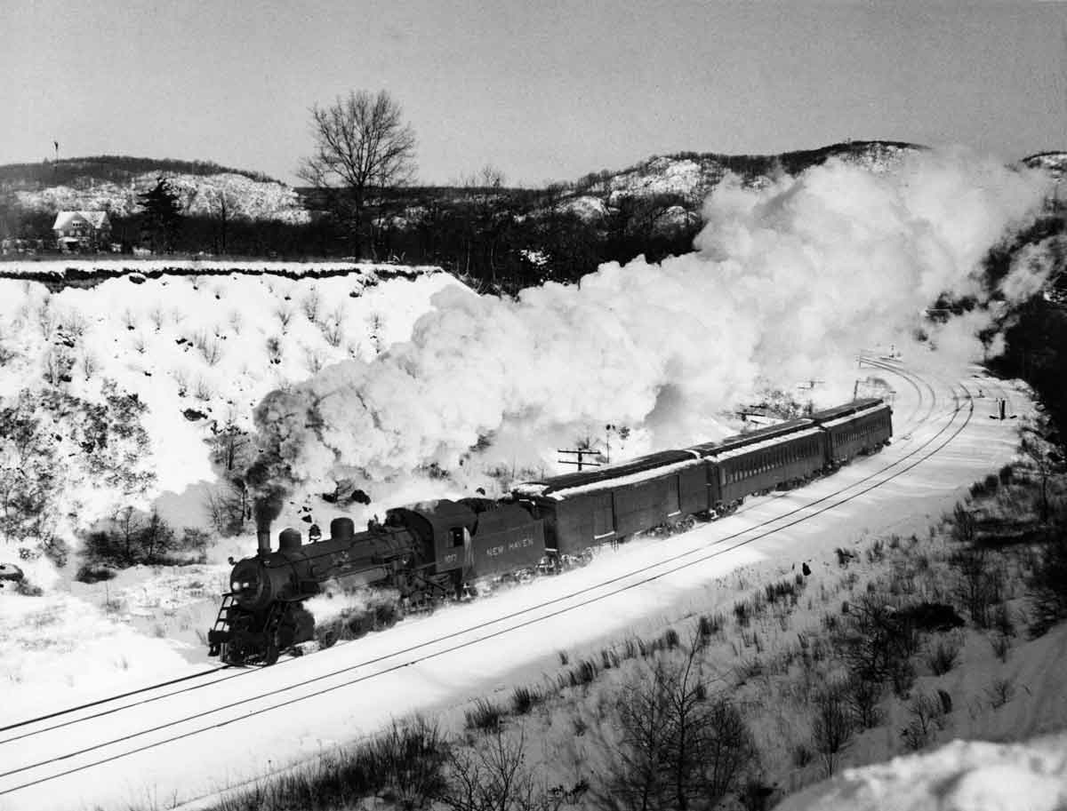 a steam passenger train rounding a curve on a winter day