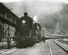 A black and white photo of a conductor posing next to a locomotive