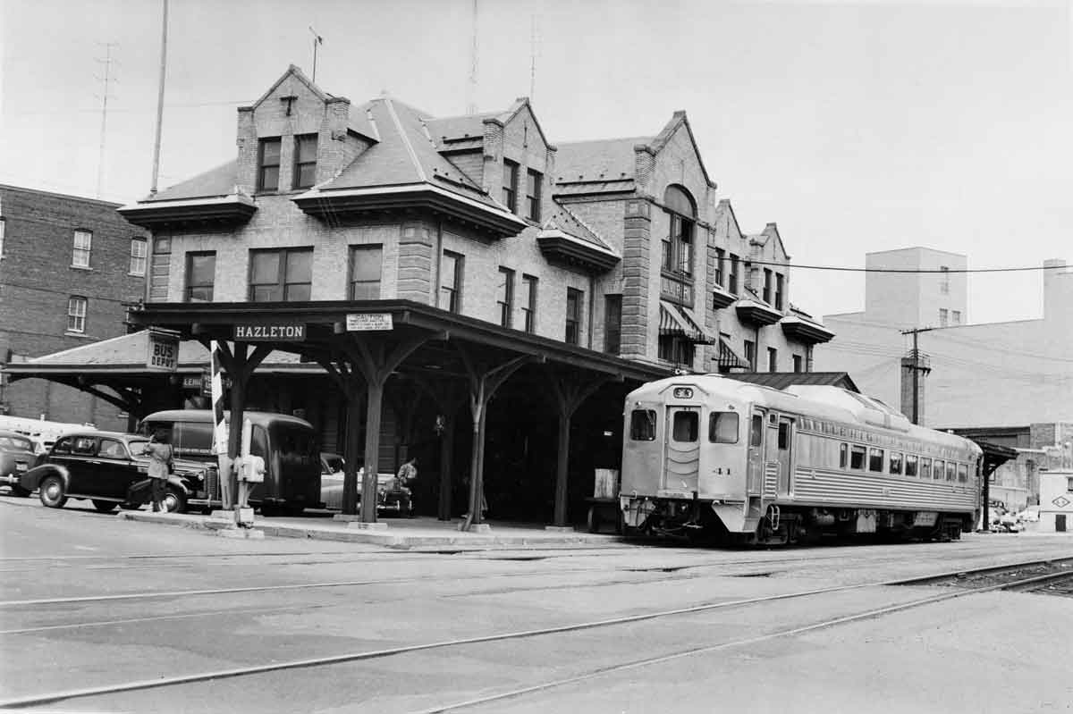 A black and white photo of a train outside a train station