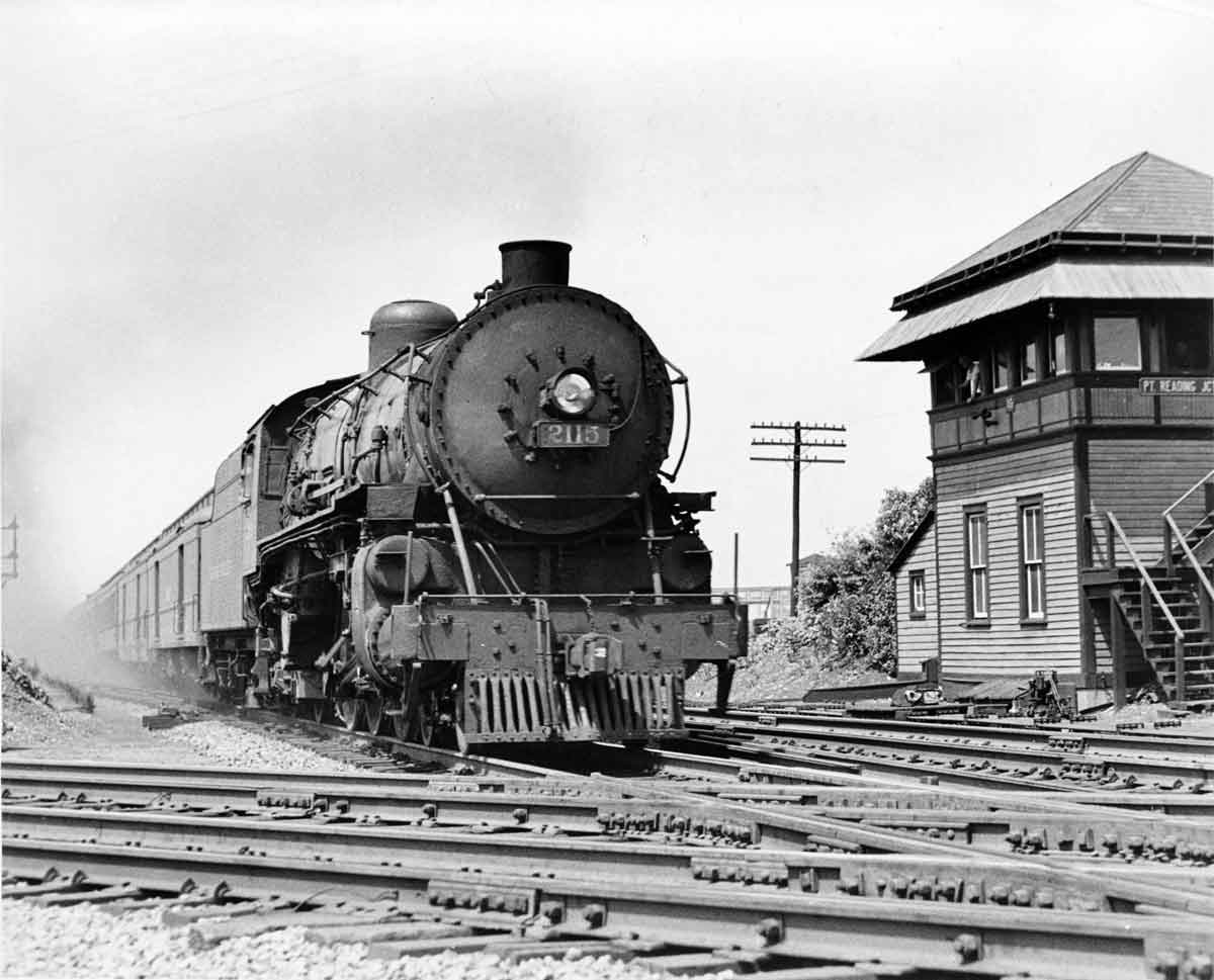 A black and white photo of a train outside a building