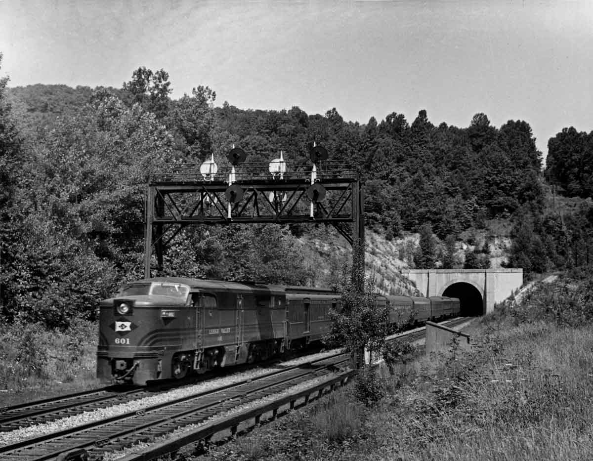 A black and white photo of a train leaving a tunnel
