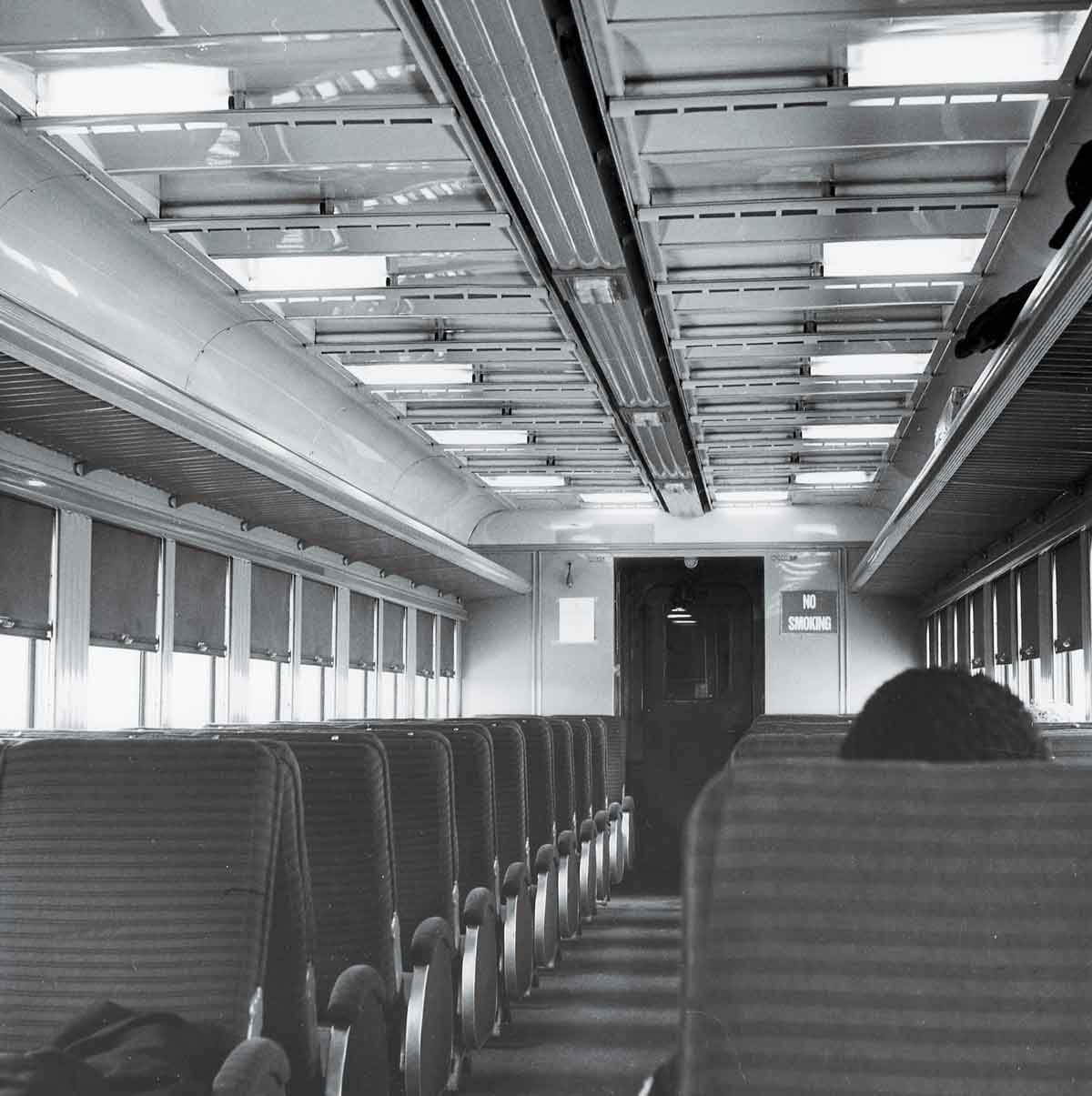 A black and white photo of the back of a passenger's head while sitting inside a train