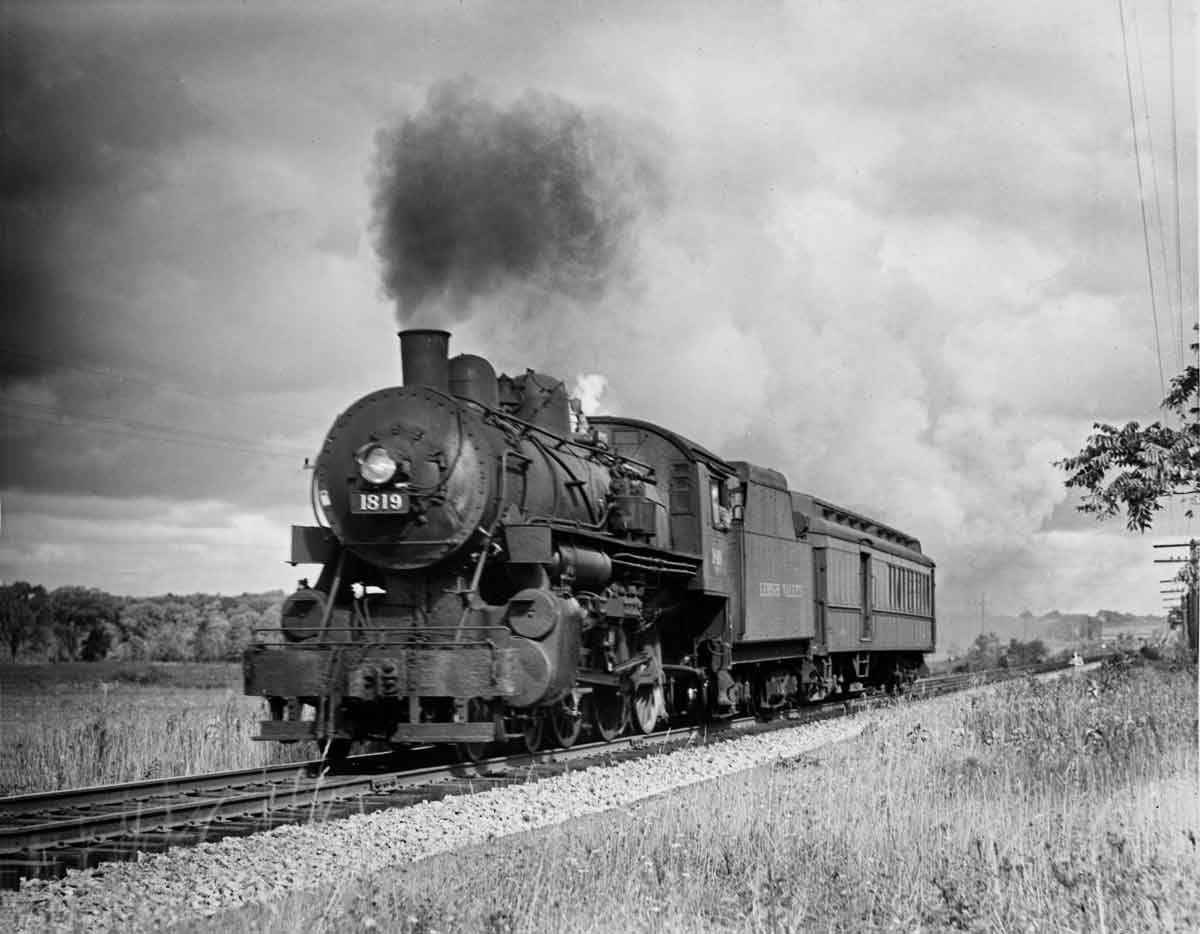 A black and white photo of a locomotive with black smoke coming out of a chimney