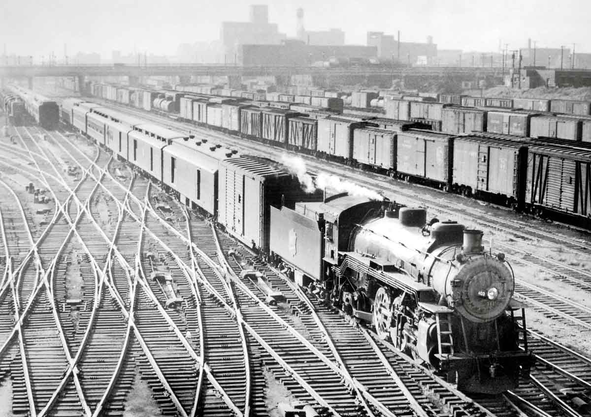 a steam engine pulling passenger cars in a rail yard