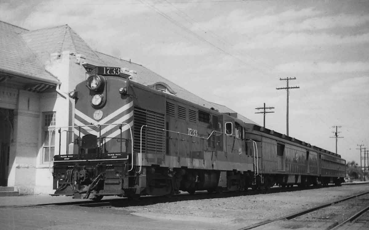 a diesel and passenger cars by a passenger depot
