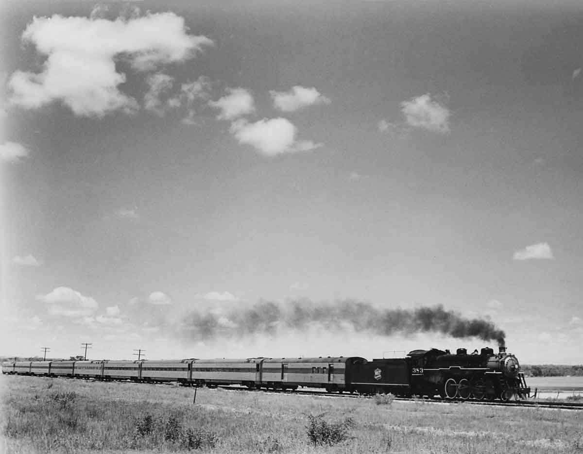 a steam engine pulling passenger cars by a field