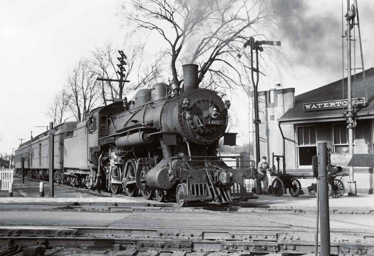 a steam engine passenger train sitting next to a train station
