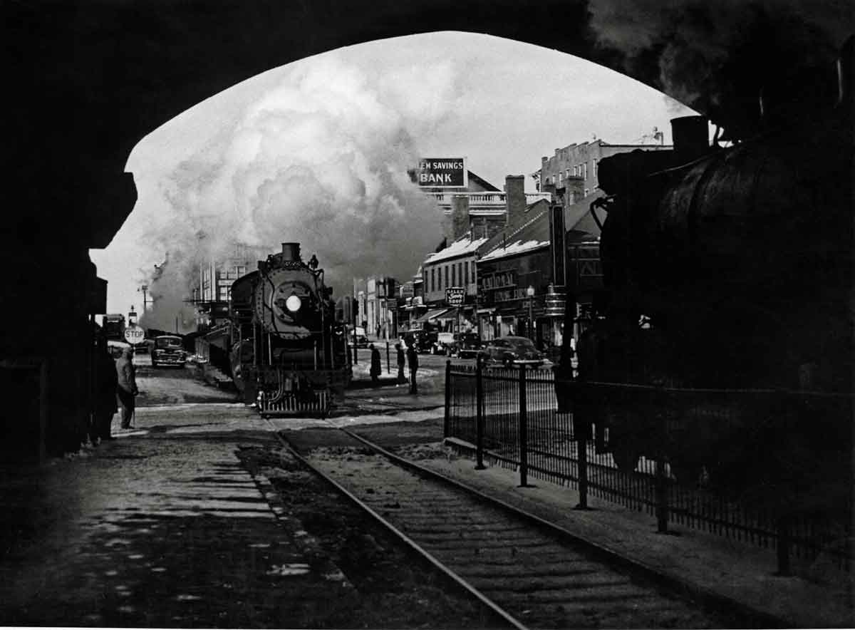 A black and white photo of a train coming toward a tunnel