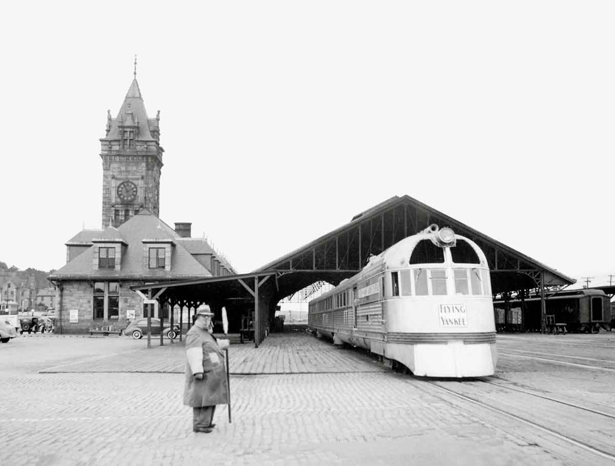 A black and white photo of a training departing the station with a person standing nearby