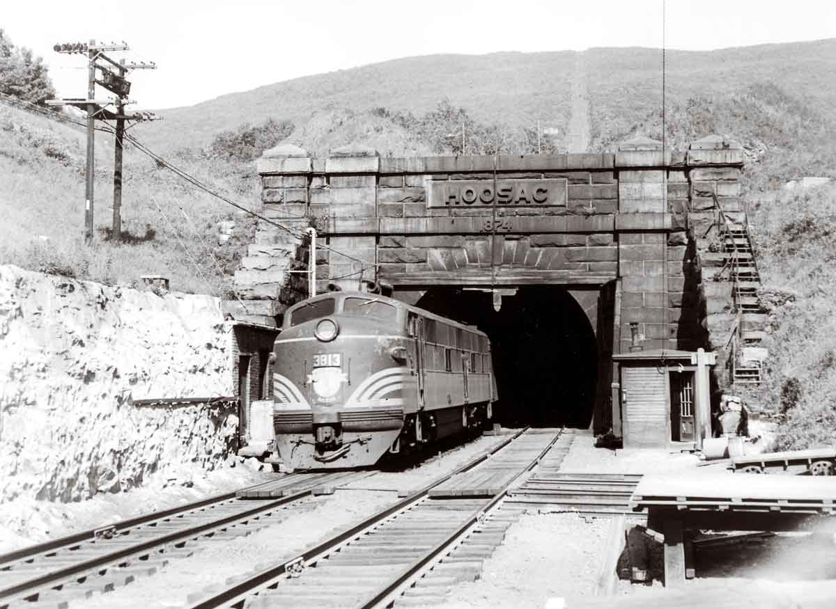 A black and white photo of a train exiting a tunnel