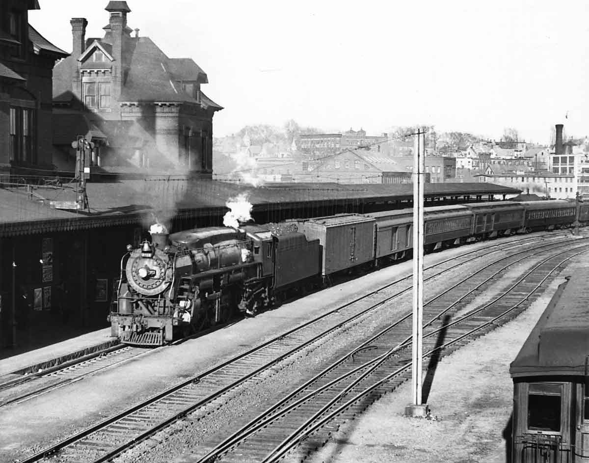 A black and white photo of a train approaching a station