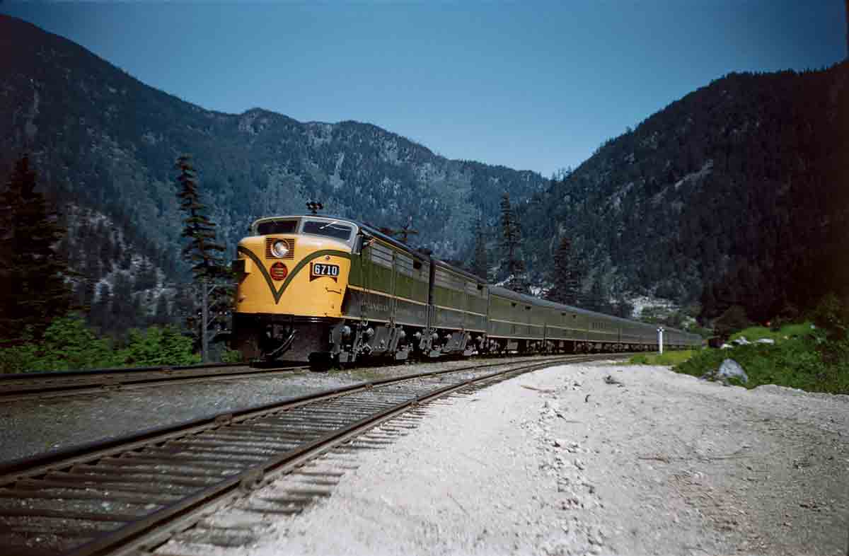 a passenger train in front of hills covered with forests