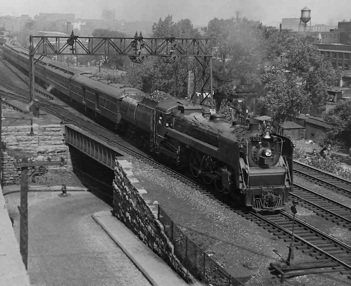 a steam engine passenger train crossing a bridge over a road