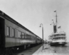 a passenger train by a body of water and a steamboat