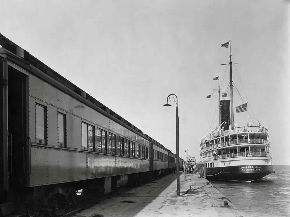 a passenger train by a body of water and a steamboat